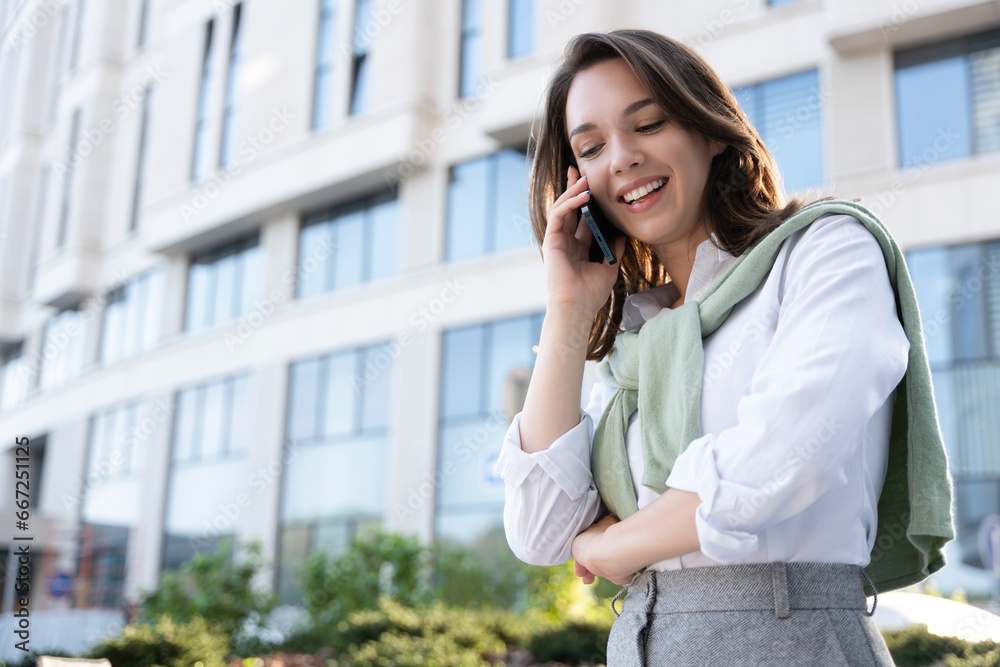 Attractive brunette businesswoman talking on mobile phone with client while standing near office building. Attractive brunette businesswoman talking on mobile phone with client while standing near office building.
