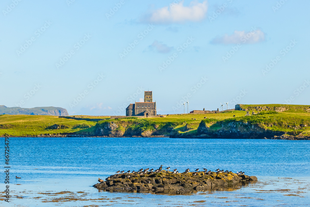 Isle of Canna, Inner Hebrides, Scotland with seabirds resting on a rock and the deconsecrated St. Edwards church on the adjoining Isle of Sanday.  Horizontal.  Copyspace