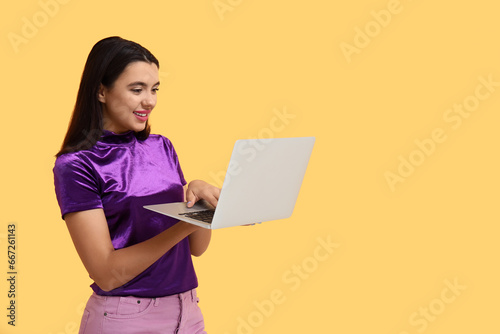 Beautiful young happy woman with laptop on yellow background