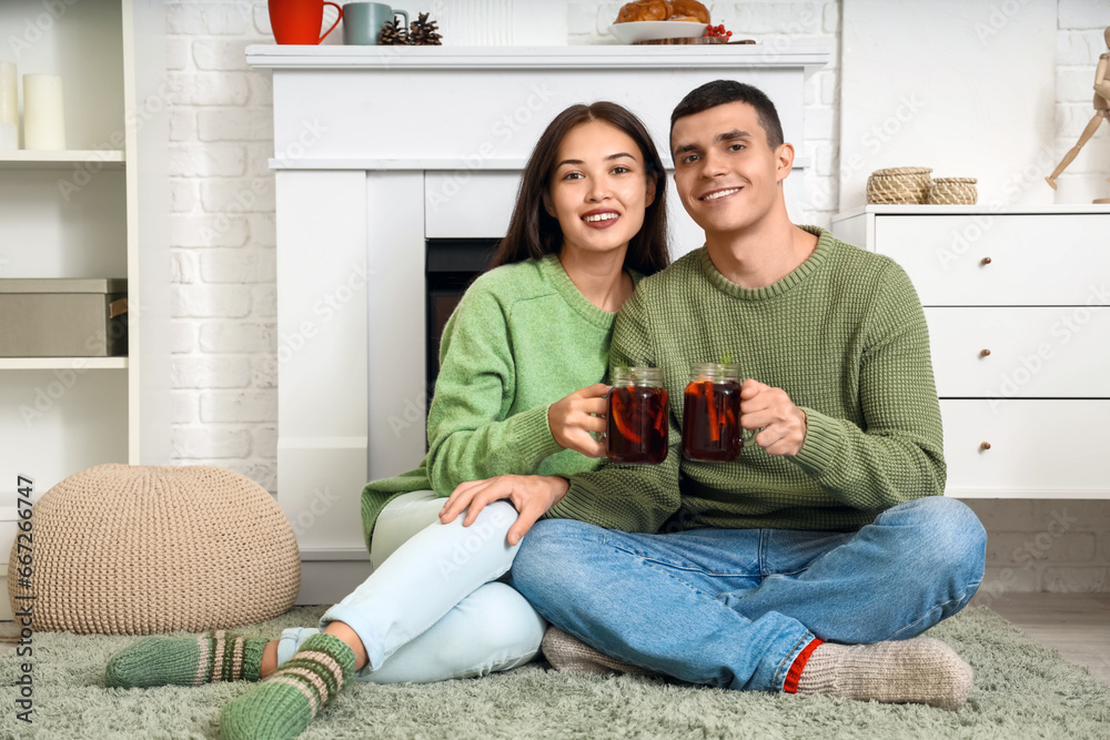 Φωτογραφία Happy couple with glasses of warm mulled wine sitting on floor in living room