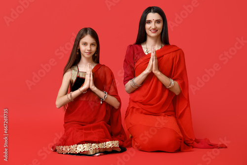 Beautiful mother with her daughter in sari on red background. Divaly celebration photo