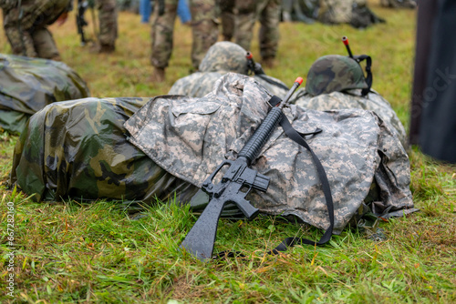 Modern black training military rifle leaning against a wet ruck backpack 