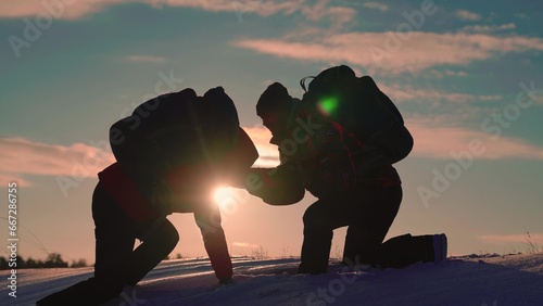 Traveler climbs snowy peak, Working in team of business people. Team of businessmen is going to win. Silhouettes of climbers give each other helping hand, climbing to top of snowy mountain, hill.
