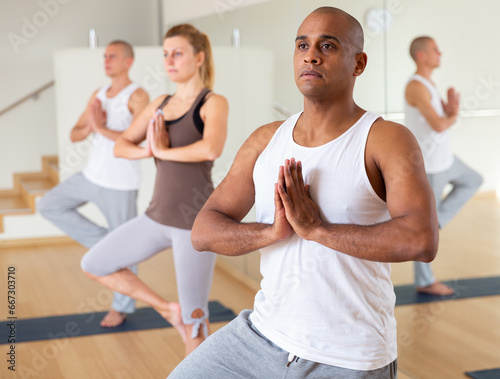 Portrait of focused man making yoga exercises with friends at fitness center