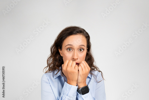 Photography Worried young woman bites fists, her eyes wide with evident fear and trepidation
