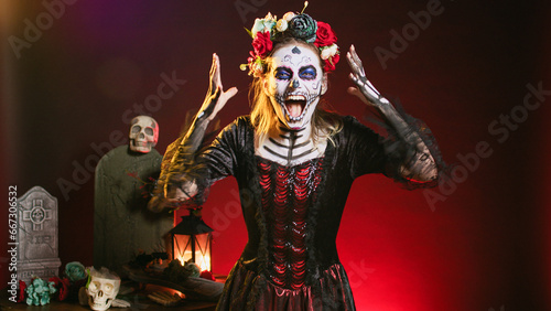 Horror goddess of death yelling in costume with skull body art, wearing flowers crown and screaming like holy santa muerte to celebrate dios de los muertos. Woman on tranditional mexican holiday.