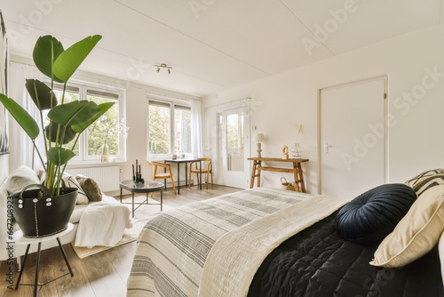 Modern bedroom with bed and houseplant against windows photo