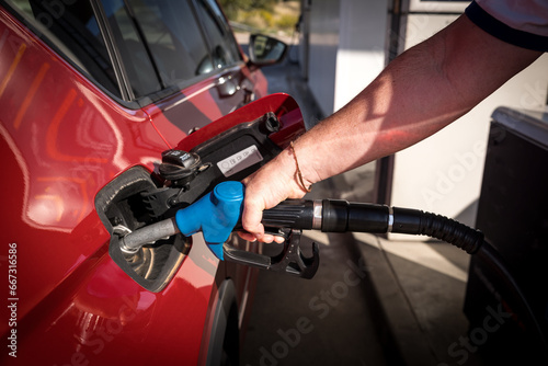 man hand refueling gasoline and filling the tank at the gas station or petrol station pump to the red car