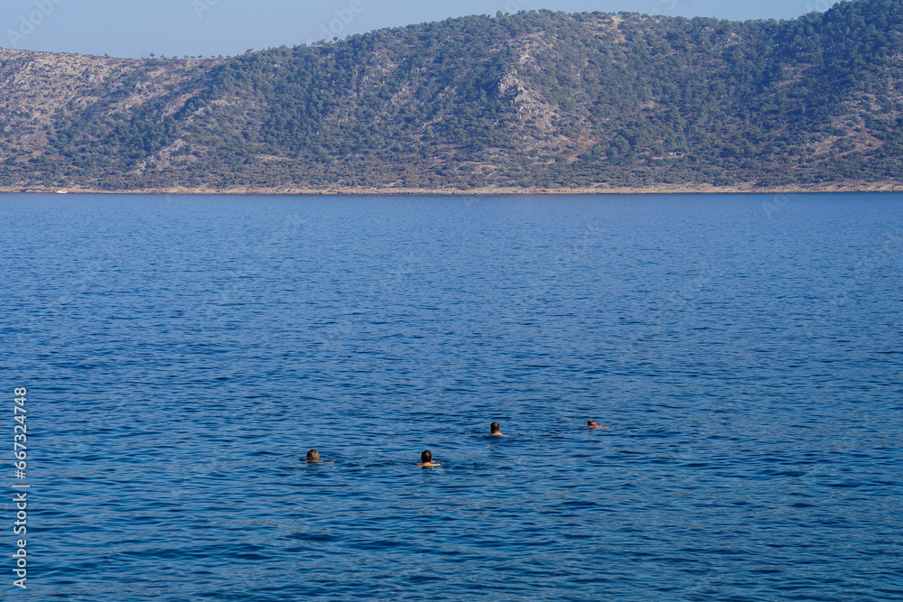 People swimming on mediterranean sea and island is far away, from back