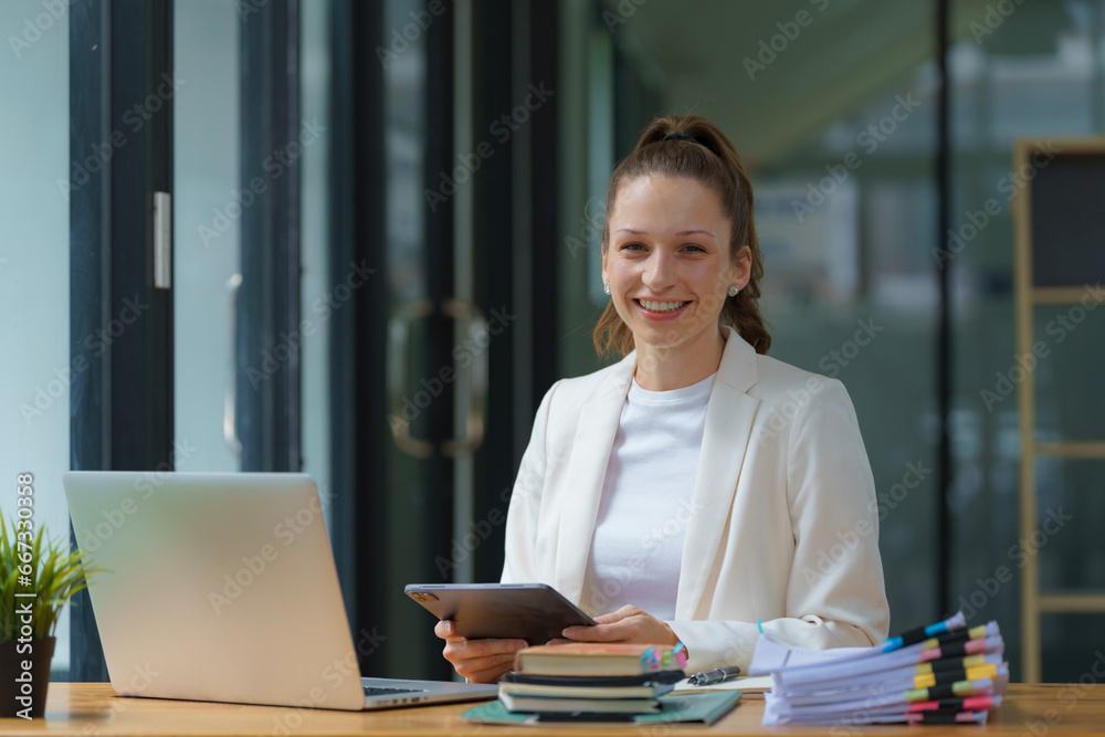 A businesswoman using a digital tablet while working with a laptop in an office. A businesswoman using a digital tablet while working with a laptop in an office.
