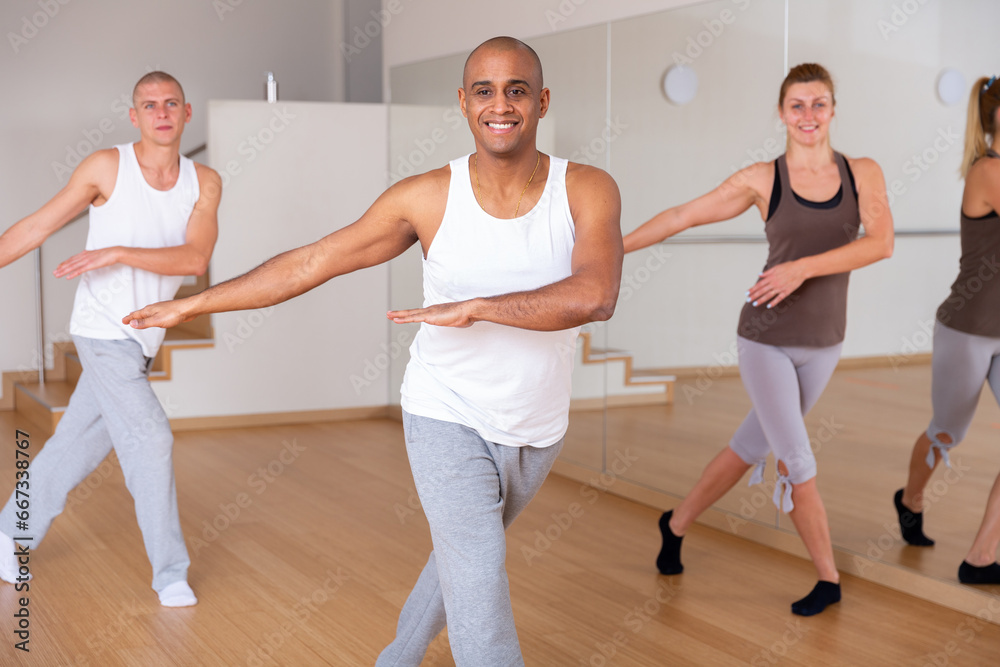 Group of happy adult people enjoying active dance in modern studio. Focus on expressive Hispanic man