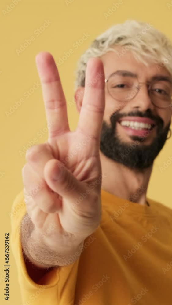 Close-up, guy showing victory sign, looking at camera isolated on yellow background Close-up, guy showing victory sign, looking at camera isolated on yellow background