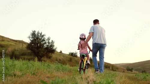 Supportive father takes care of preschooler girl learning to ride bicycle in field