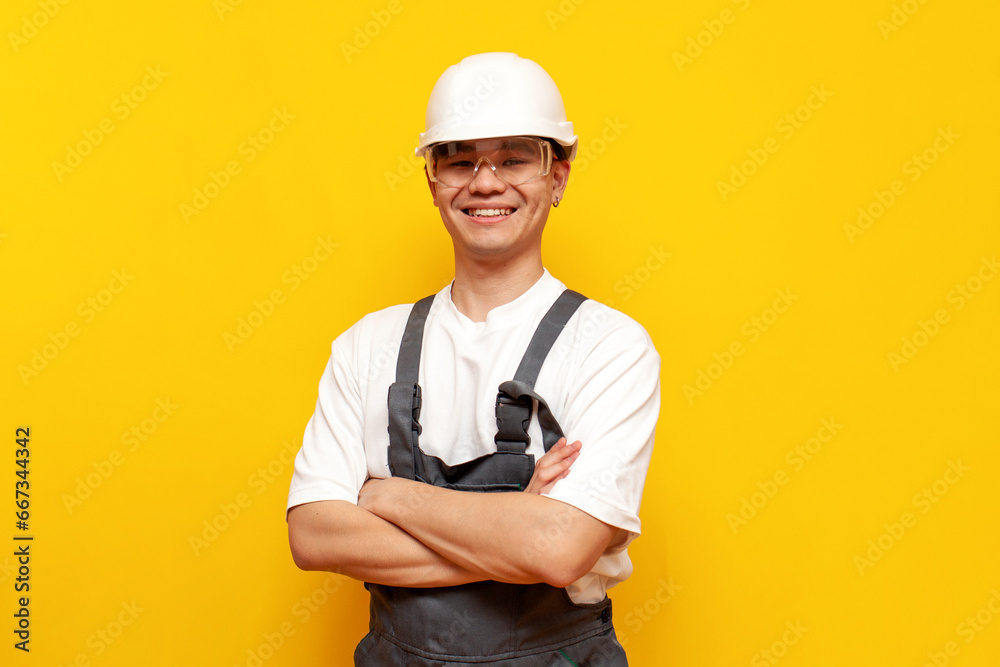 asian male builder in uniform standing with arms crossed and smiling on yellow isolated background asian male builder in uniform standing with arms crossed and smiling on yellow isolated background
