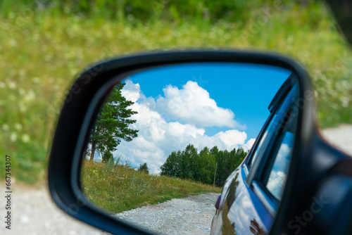 Fotografi Summer countryside landscape in the rearview mirror of a car during a trip