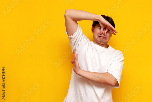 young asian guy in a white t-shirt covers his nose from the unpleasant odor from his armpits avoids and refuses photo