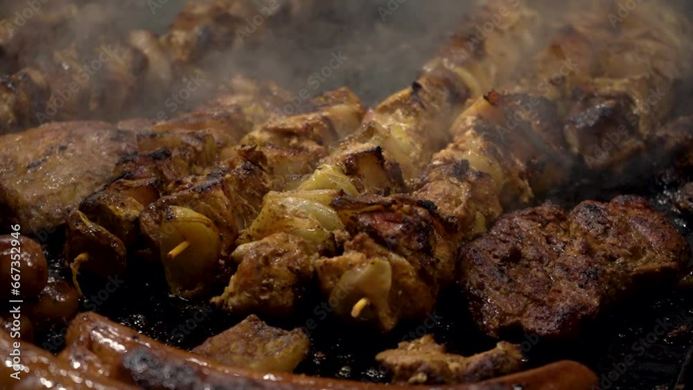 Close-up of cooking kebab,meat, sausages and steak on grill,on an open fire in evening at traditional street food festival.Festive fair on main square of city,cooking delicious meat on fire in smoke. Close-up of cooking kebab,meat, sausages and steak on grill,on an open fire in evening at traditional street food festival.Festive fair on main square of city,cooking delicious meat on fire in smoke.