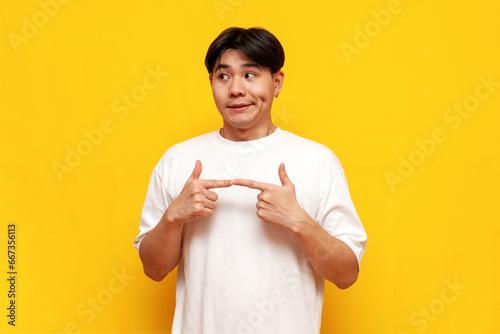 Foto modest young asian guy in white t-shirt feeling shy on yellow isolated backgroun