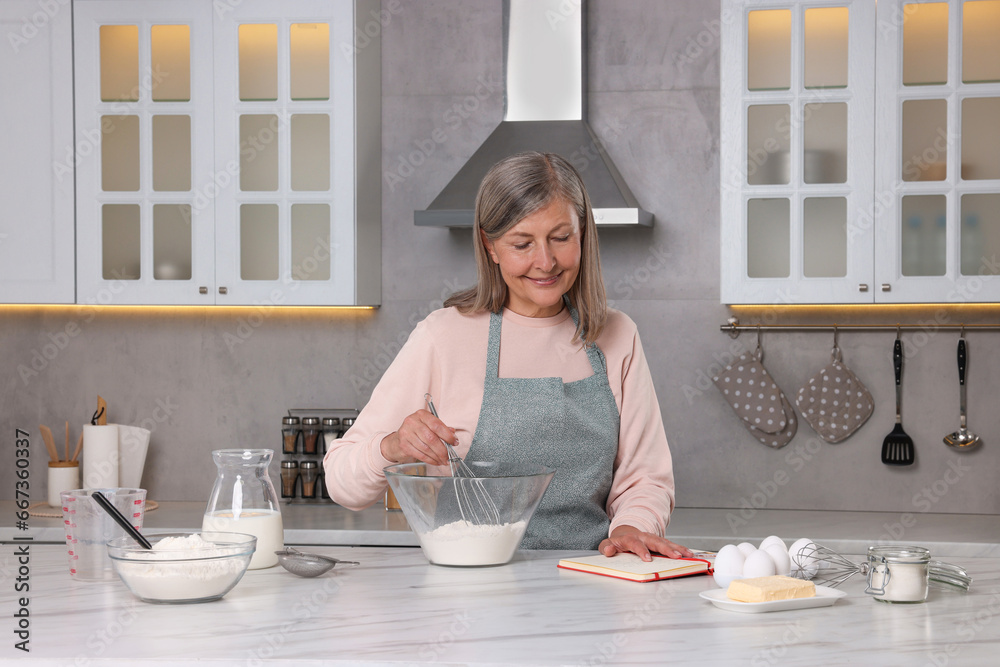 Senior woman with recipe book cooking in kitchen Senior woman with recipe book cooking in kitchen