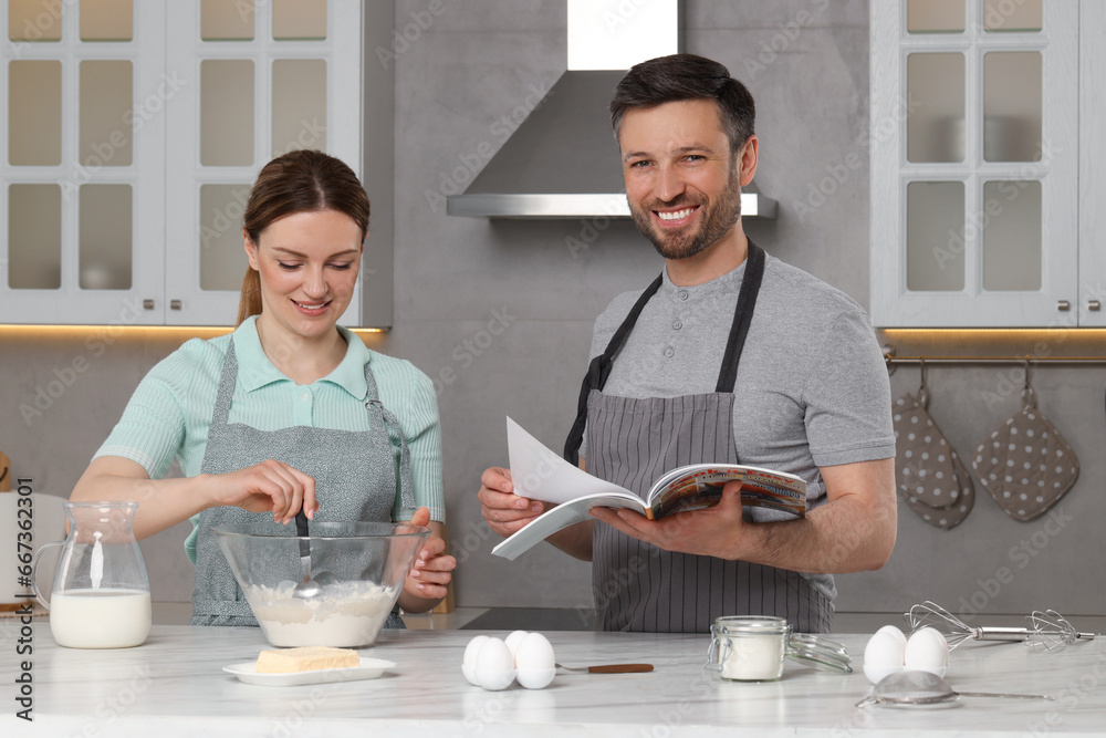 Happy couple reading recipe in culinary magazine while cooking at home Happy couple reading recipe in culinary magazine while cooking at home