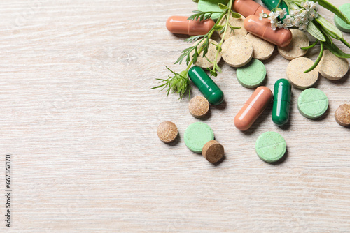 Different pills and herbs on wooden table, above view with space for text. Dietary supplements