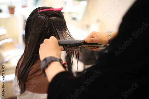  女性の髪にヘアアイロンをかける男性美容師