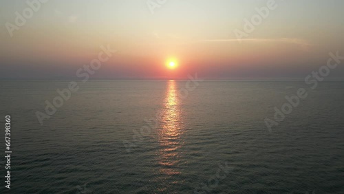 Aerial view of sunset or sunrise on the ocean with calm wave in Bali. Dusk or dawn on the beach with clear sky. Sunlight reflection on middle of the sea. Wide angle cinematic for opening ending scene.