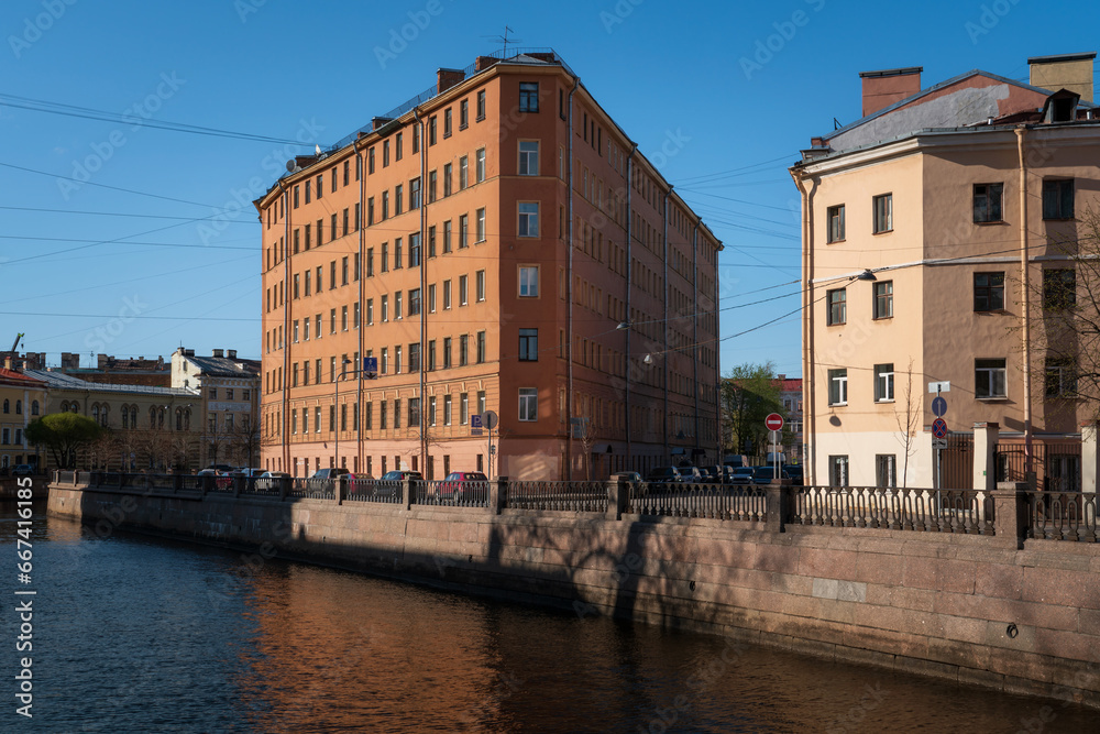View of a residential building in the shape of an iron on the embankment of the Griboyedov Canal on a sunny day, St. Petersburg, Russia