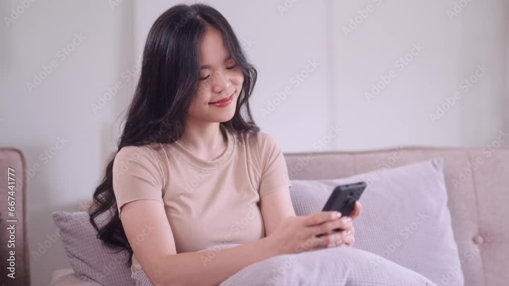 young Asian woman hand holding smartphone sitting on the couch watching funny videos at home, Wireless communication and networking concept. young Asian woman hand holding smartphone sitting on the couch watching funny videos at home, Wireless communication and networking concept.