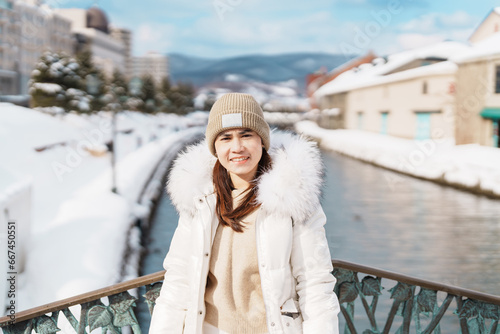 Woman tourist Visiting in Otaru, happy Traveler in Sweater sightseeing Otaru canal with Snow in winter season. landmark and popular for attractions in Hokkaido, Japan. Travel and Vacation concept