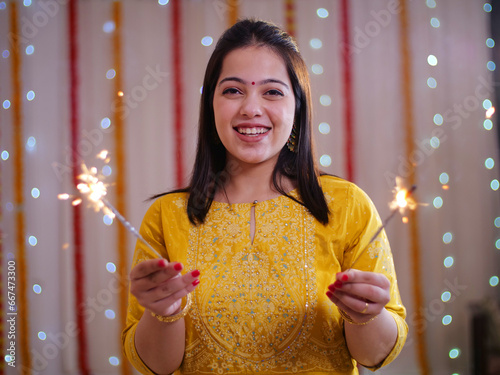 Beautiful young Indian woman having fun with firecrackers in traditional clothing - Diwali festival. Attractive Indian female bursting pencil crackers (phuljhadi) and dancing while celebrating Dipa... photo