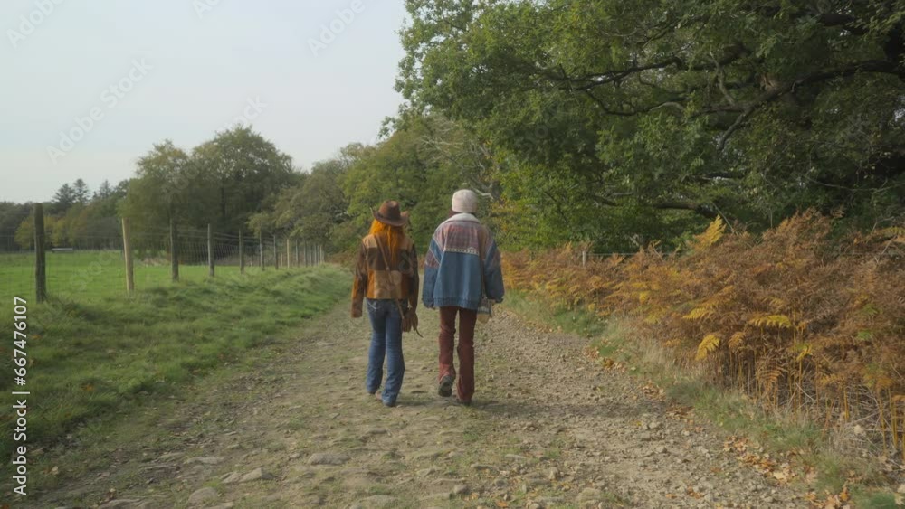 Two young women walking along English countryside track on bright autumn day with woodland. Half speed slow motion. Quarter stop pro mist filter. Two young women walking along English countryside track on bright autumn day with woodland. Half speed slow motion. Quarter stop pro mist filter.