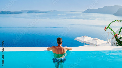 a young men in swim shorts relaxing in the pool looking out over the caldera of Santorini Island Greece, man at an infinity pool, a young guy on a luxury vacation in Europe Greece.