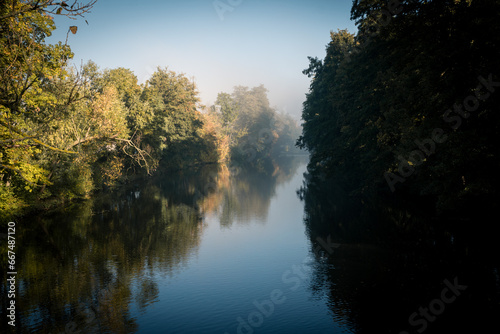 Autumn morning by the river, sunbeams shining through colorful trees