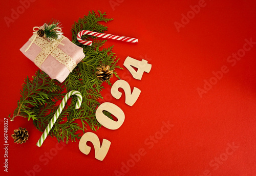 Christmas frame with a branches of thuja and gifts on a red background. Winter holidays. Space for text. Top view, flat lay. Christmas. Template, layout. A greeting card with numers 2024 photo