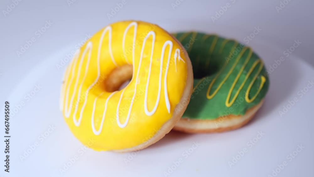 Two donuts with green and yellow glazing with cream and white chocolate fudge rotate on white surface. Delicious baked sweet buns. Colorful appetizing tasty confectionery.