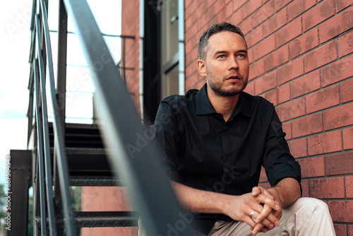 Businessman sitting on a ladder in a dark room, young man portrait