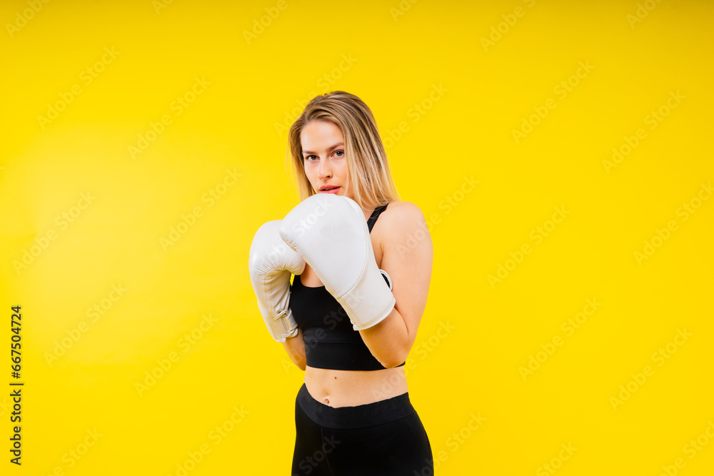 Woman boxer in gloves training on yellow and dark studio background Woman boxer in gloves training on yellow and dark studio background