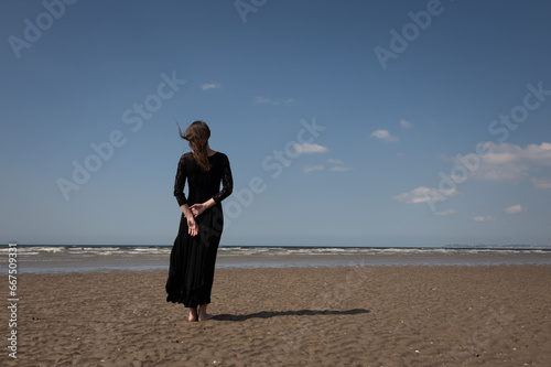 rear view of woman in long black dress standing alone on beach