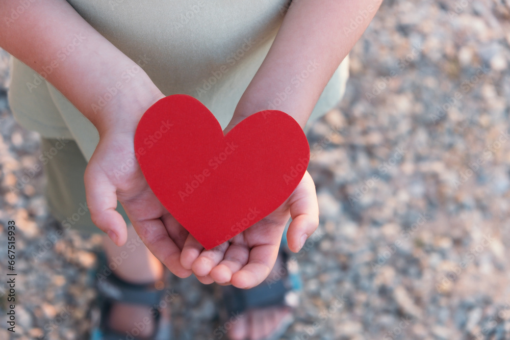 Fototapeta premium Child holding red heart. Heart health, charity and hope concept. Top view