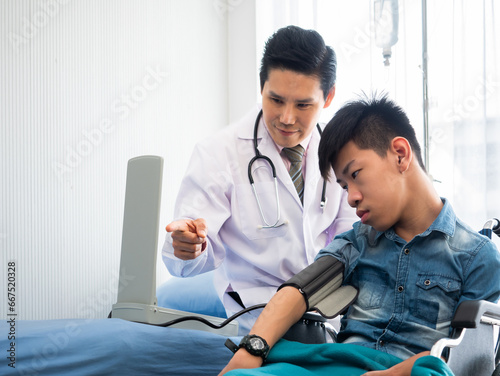 Asian kid doctor check blood pressure on young disabled child arm and point finger to measure number with explain about the item in check up room at the clinic center photo