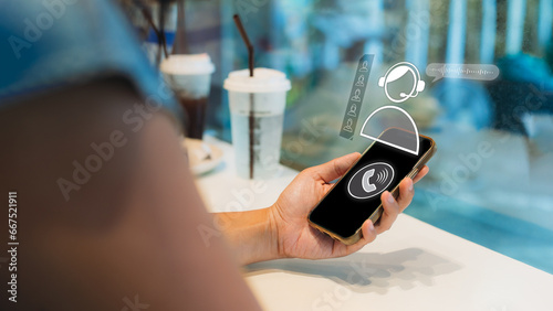 Businesswoman hand holding a smartphone with virtual screen of ringing phone receiver and phone call icon at the cafe. Conversation assistant, digital chatbot virtual screen. AI system.
