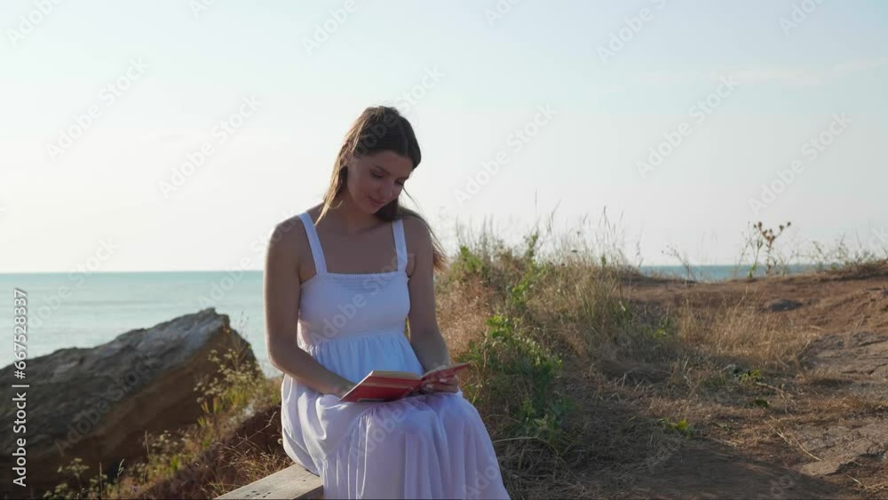 Beautiful woman reading book on wooden bench near sea at sunrise. Camera moving backward