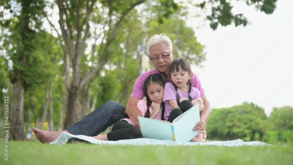 Happy Asian family children reading a book with her grandfather in the park Happy Asian family children reading a book with her grandfather in the park