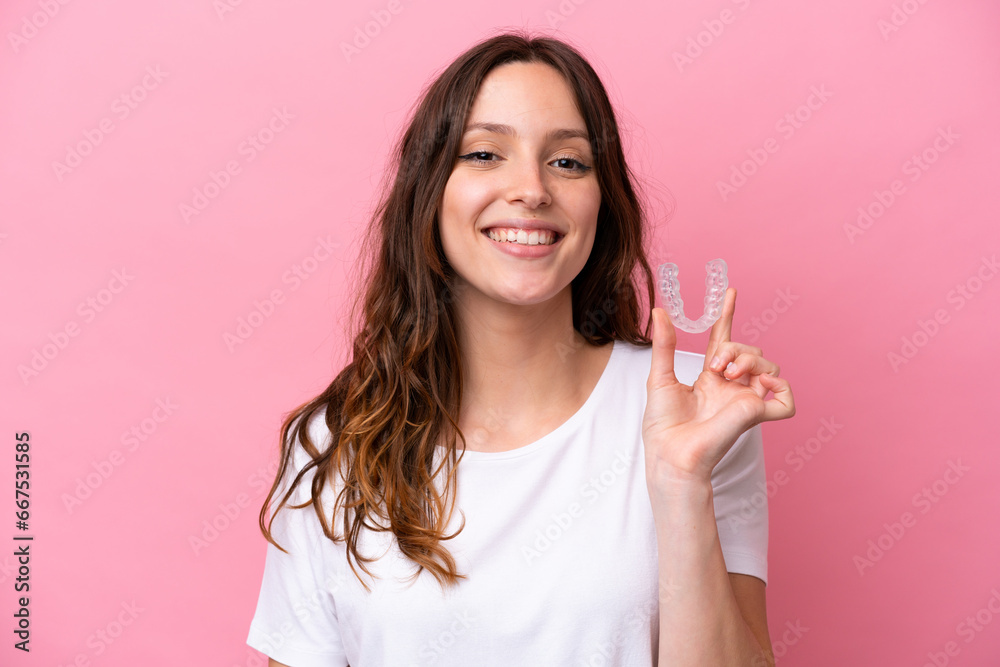 Young caucasian woman holding invisible braces isolated on pink background smiling a lot Young caucasian woman holding invisible braces isolated on pink background smiling a lot