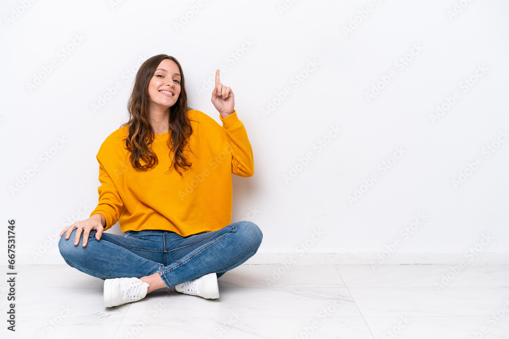 Young caucasian woman sitting on the floor isolated on white wall showing and lifting a finger in sign of the best Young caucasian woman sitting on the floor isolated on white wall showing and lifting a finger in sign of the best