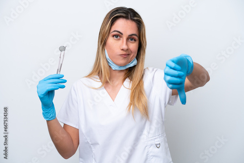 Dentist woman holding tools isolated on white background showing thumb down with negative expression