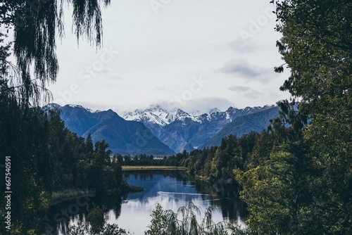 Tranquil lake surrounded by lush evergreen trees with majestic snow-capped mountains in New Zealand