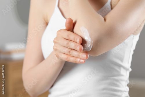Woman applying body cream onto elbow indoors, closeup
