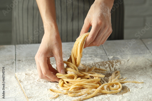 Woman with homemade pasta at light tiled table, closeup
